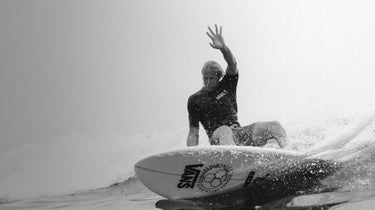 Man surfing an epic wave in black and white with a raen logo on the board