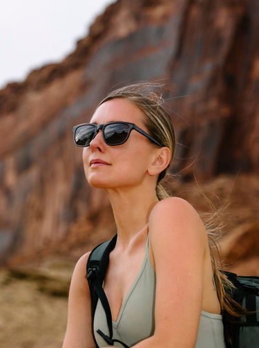 Woman wearing sunglasses and a tank top with a backpack in a desert setting