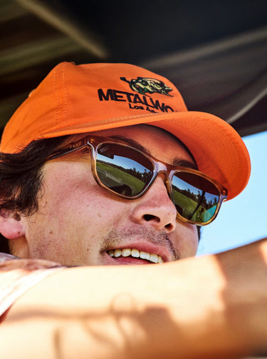 Person wearing an orange cap with a logo and sunglasses, outdoors.