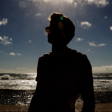 Silhouette of a person on a beach with ocean waves and sky.